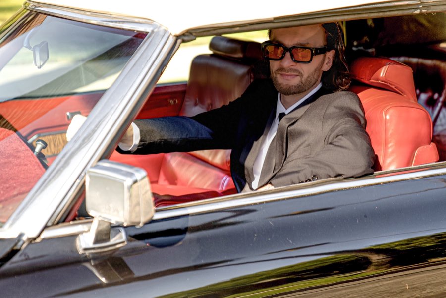 Chrome mirror and red interior of the black Cadillac convertible, a man in a dark suit at the wheel