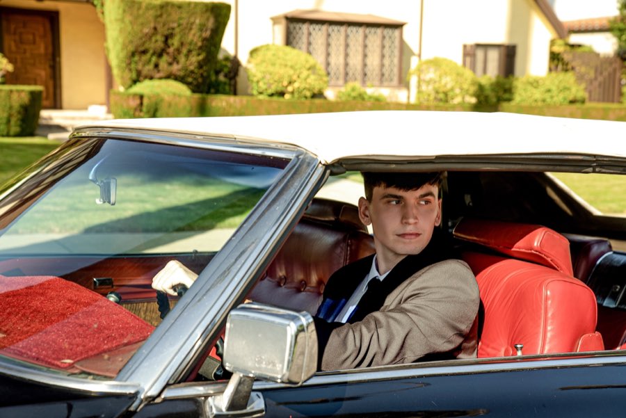 Red interior of the black Cadillac DeVille seen through the window, a young man in a suit at the wheel