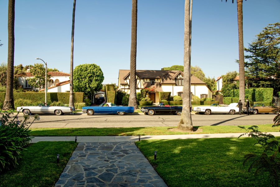 Vintage Cadillacs lined up on a palm-lined Los Angeles street, including the blue and the black convertible