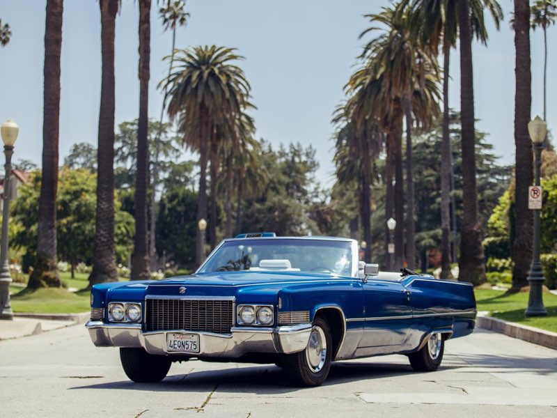Blue 1970 Cadillac DeVille convertible, roof down, on a palm-lined street in Los Angeles