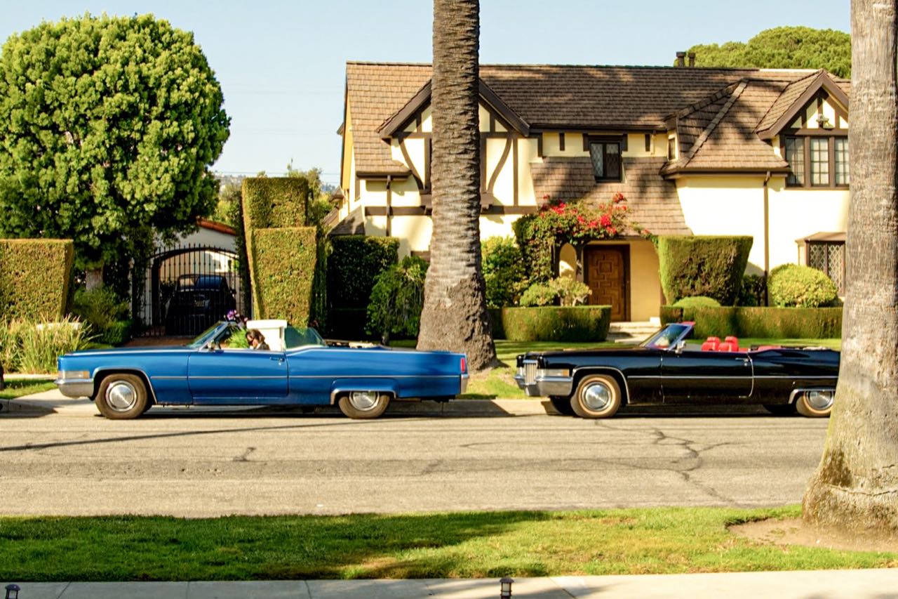 Blue and black 1970 Cadillac DeVille convertibles parked on a palm-lined Beverly Hills street