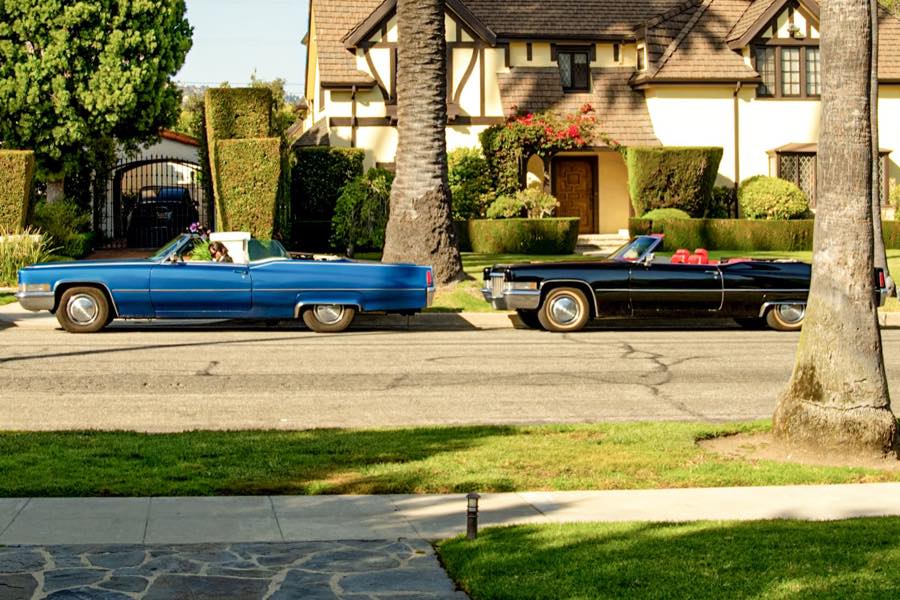 The blue and the black 1970 Cadillac DeVille convertibles, roof down, parked outside a Tudor-style house in Los Angeles