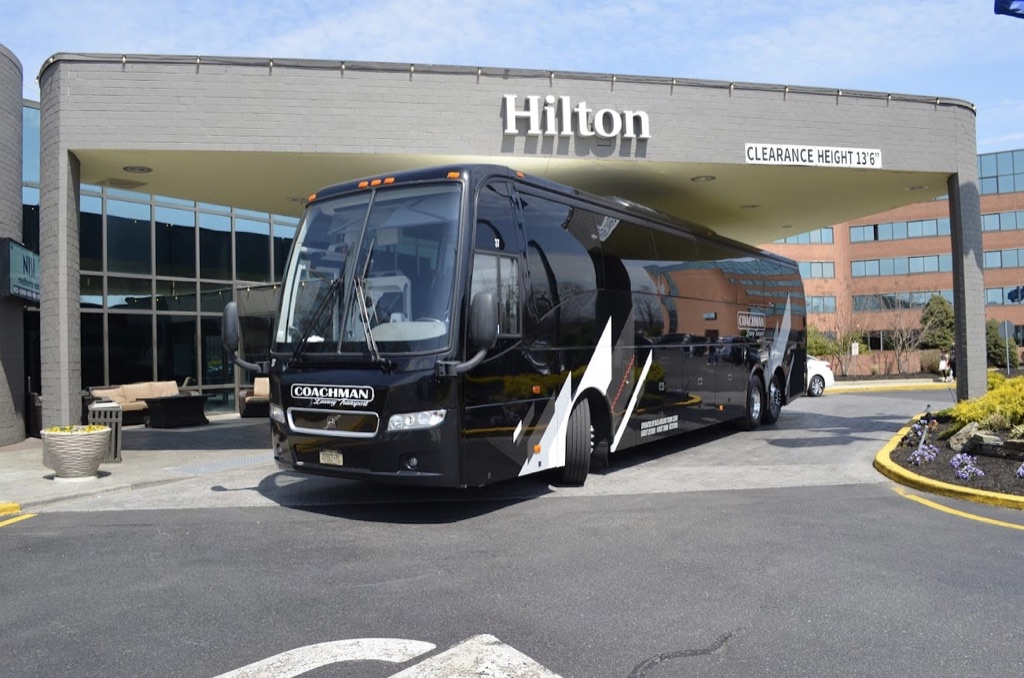 Black charter coach bus parked under a hotel entrance canopy