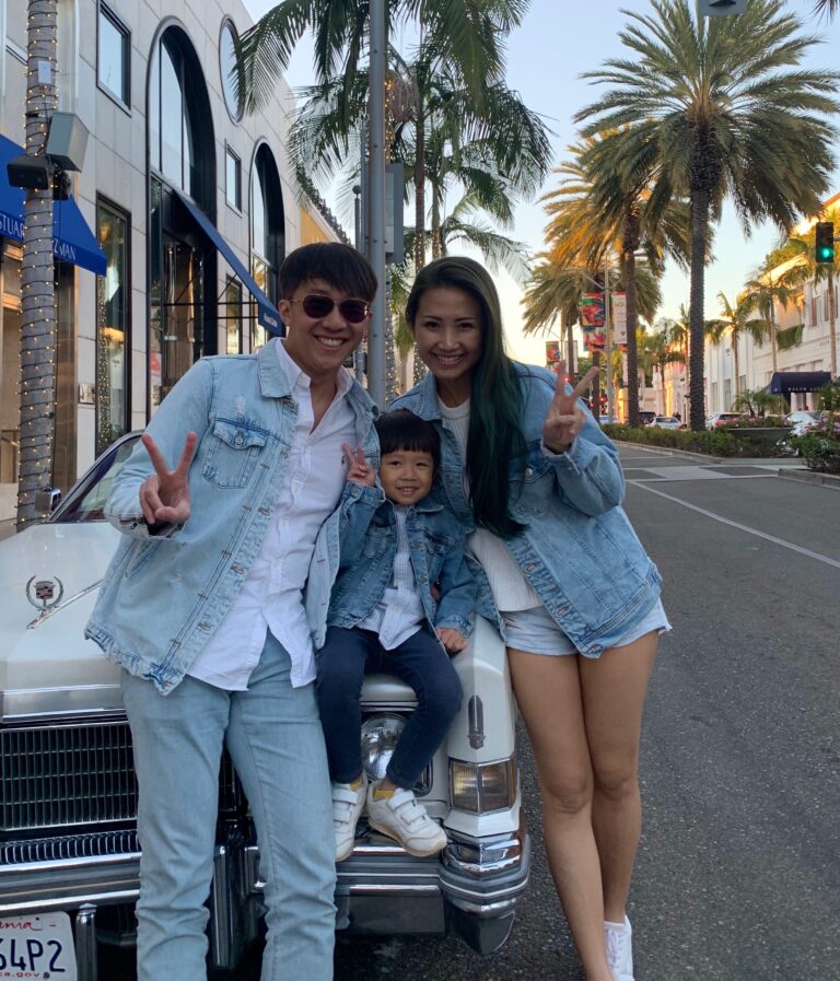 Two adults and a child posing with a white vintage Cadillac on Rodeo Drive