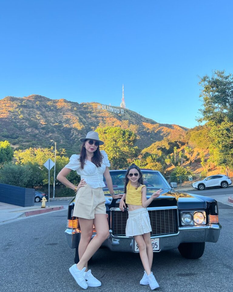 A woman and a girl with the black Cadillac below the Hollywood Sign