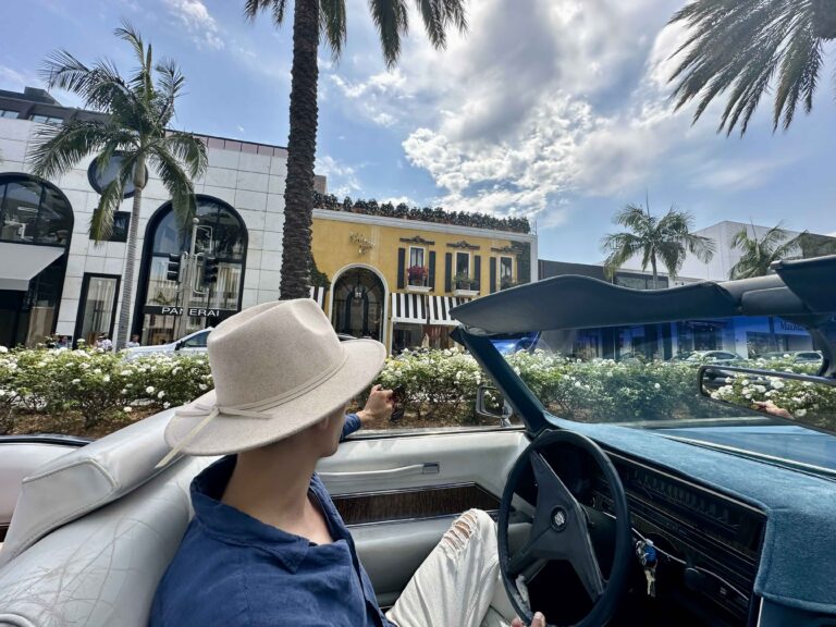 A guest in a sun hat riding in the blue convertible on Rodeo Drive, Beverly Hills