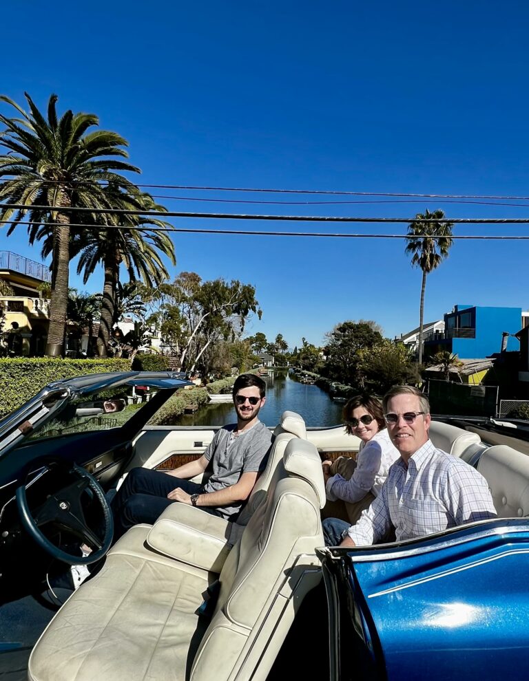 Three people in the white seats of the blue Cadillac by the Venice canals