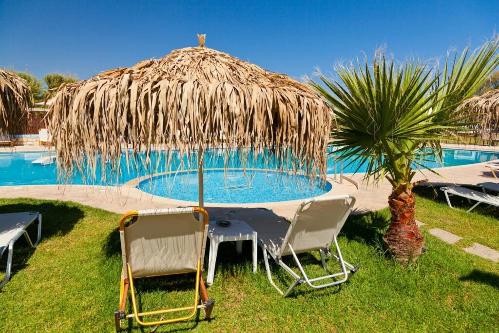 Hotel pool with thatched umbrellas, lounge chairs and a small palm