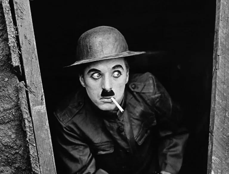 Charlie Chaplin in a bowler hat with a cigarette, peering through a doorway