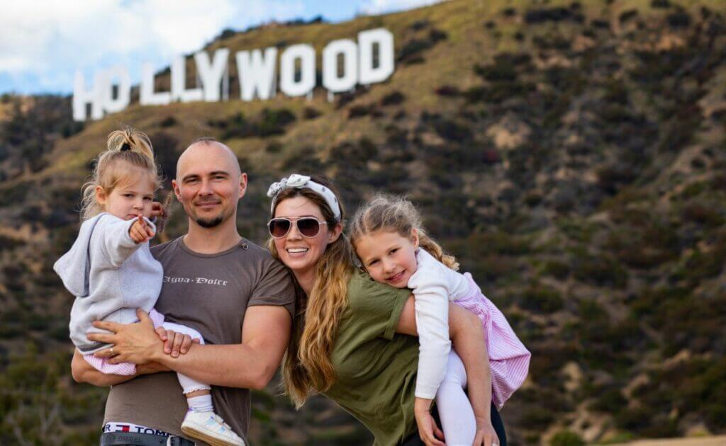 A family with two young girls posing in front of the Hollywood Sign