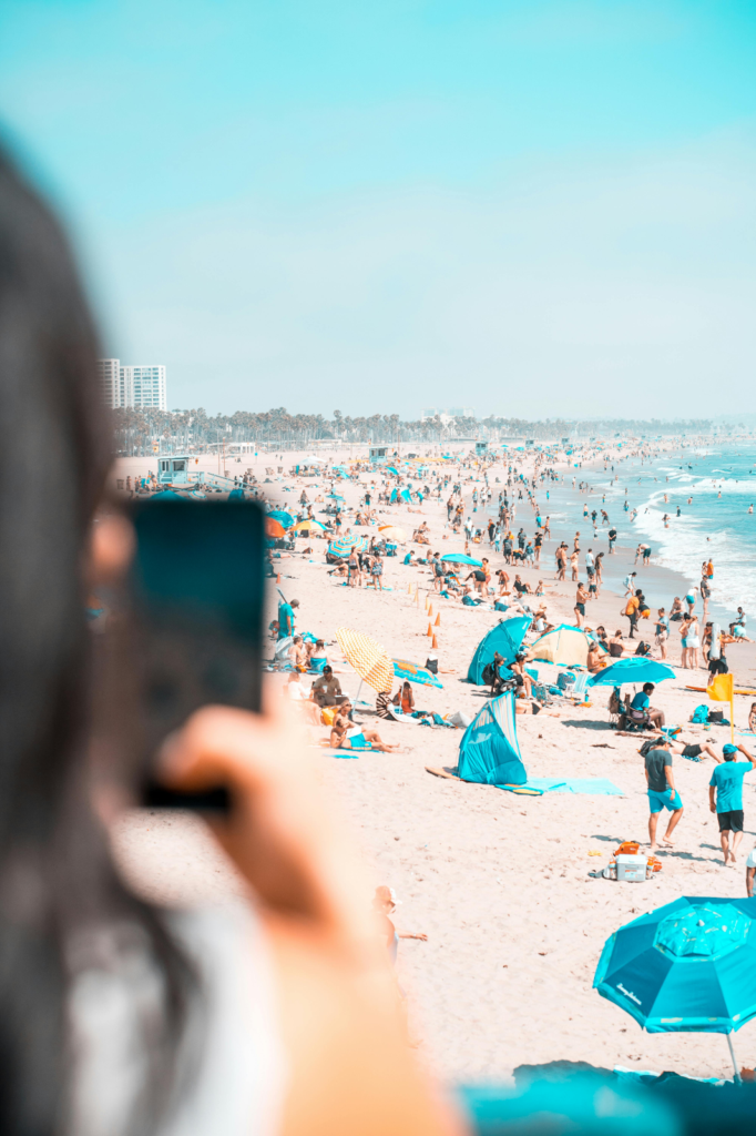 A woman photographing a crowded beach with blue umbrellas on her phone
