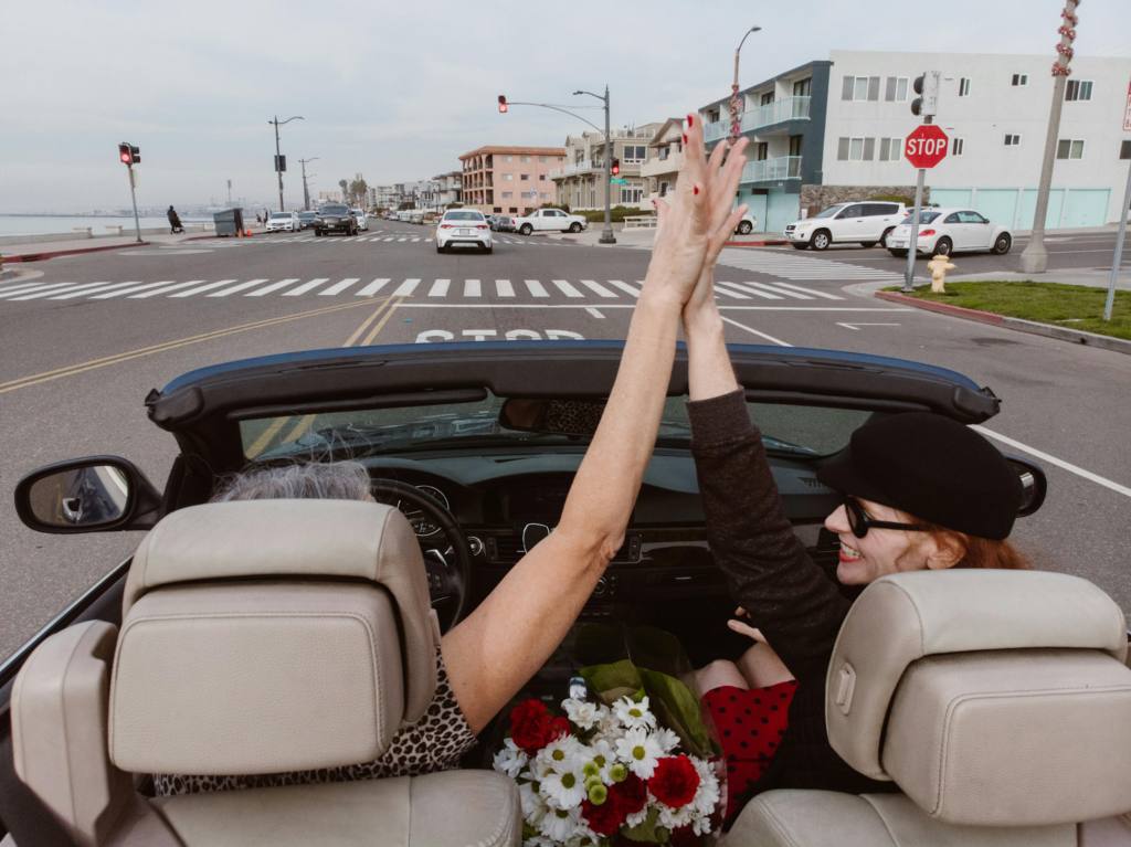 Two friends raising their hands in a convertible with a bouquet of flowers
