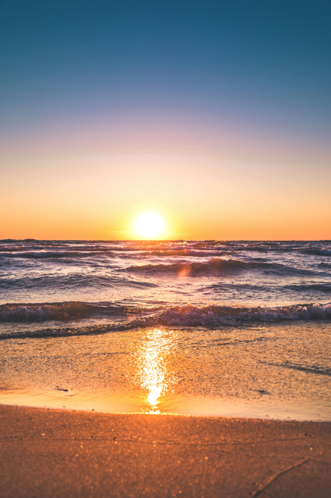 The sun setting over waves rolling onto a sandy beach