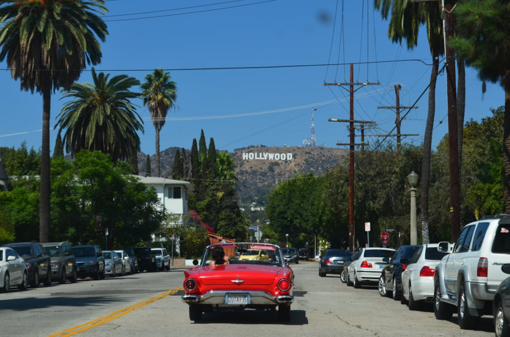A red vintage Thunderbird convertible on a residential street with the Hollywood Sign beyond